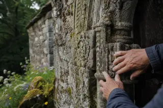 Close-up of an artisan's hands tracing ancient carvings on a mossy Romanesque chapel doorway at sunrise, surrounded by wildflowers and soft forest shadows.